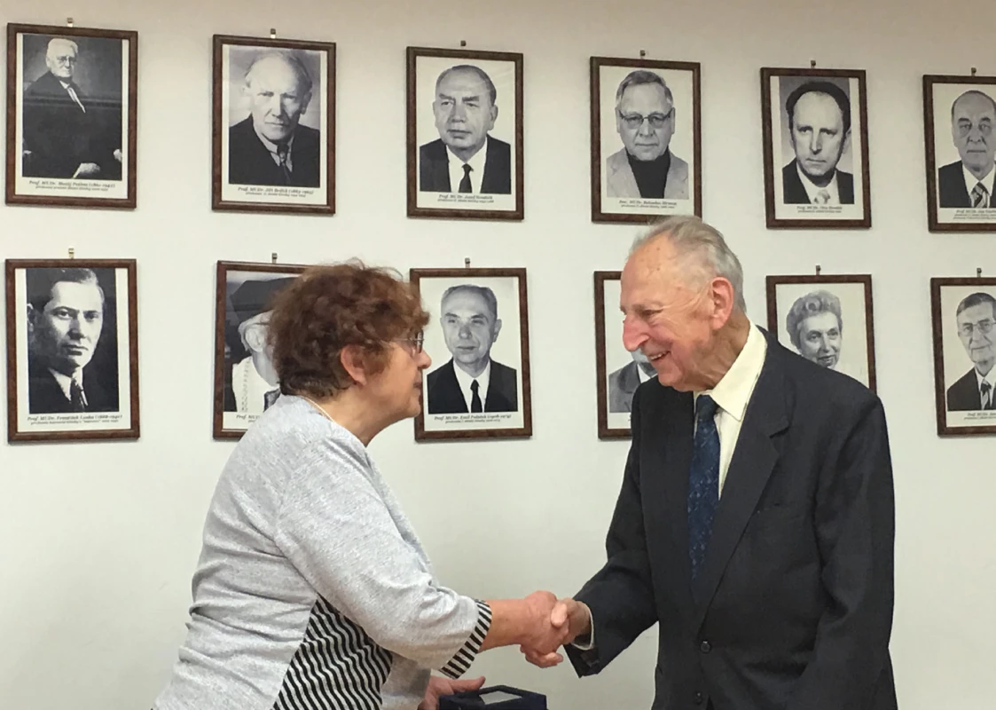 Profesor Hrodek přebírá z rukou docentky Marešové Zlatou medaili ČLS JEP na zasedání výboru České pediatrické společnosti dne 13. 4. 2017. V pravém horním rohu stěny fotografie profesora Hrodka jako přednosty II. dětské kliniky v roce 1989.