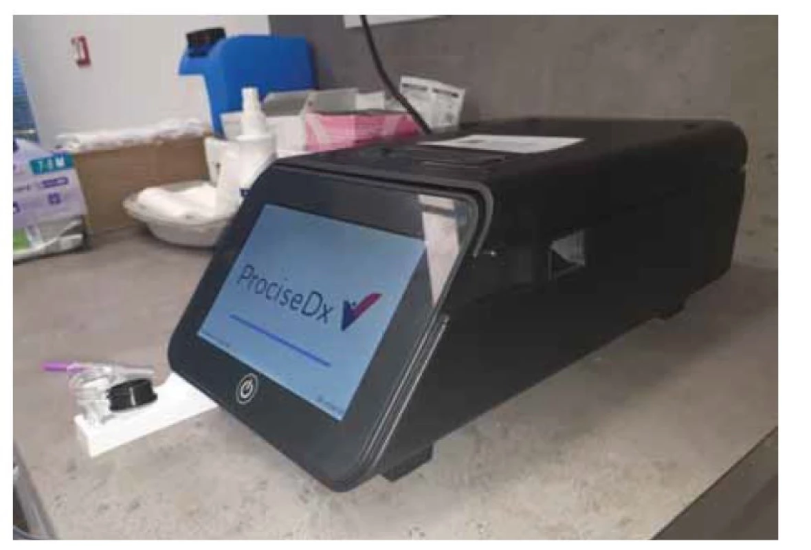 Stolní analyzátor ProciseDx k point-of-care měření údolních koncentrací
(trough levels) infiximabu a adalimumabu, reakční kyveta a mikropipeta
k odběru kapilární krve.<br>
Fig. 1. ProciseDx analyser for point-of-care measurement of trough levels of infiximab
 and adalimumab, reaction cuvette and micropipette for capillary blood
collection.